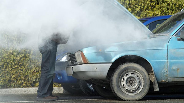 A man inspecting an Industrial Grade car with smoke coming out of the hood.