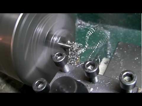 Metal lathe in operation, machining a steel rod, with metal shavings spiraling off the workpiece.