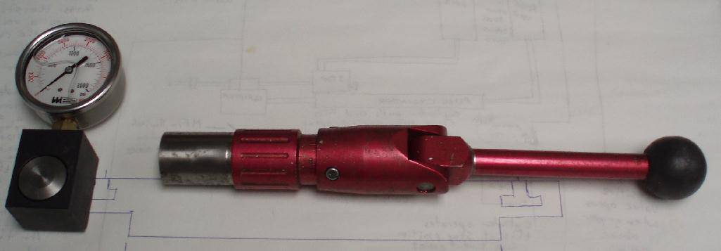 A red torque wrench with a black handle laid on a blueprint. a pressure gauge and a black metal block are also visible on the blueprint.