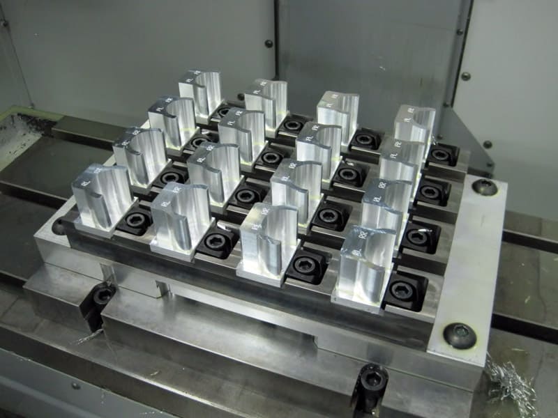 Multiple metal parts organized on a machining fixture inside an industrial machine.