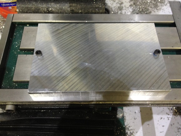 Metal plate with two holes on each side, on a green surface.