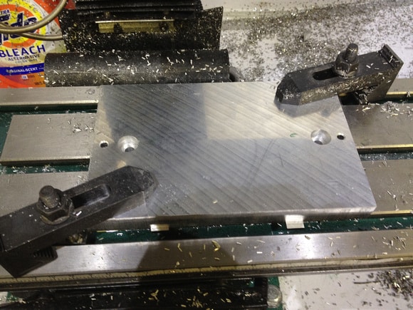 Metalworking setup featuring milling machine or lathe with aluminum plate, tools, and debris.