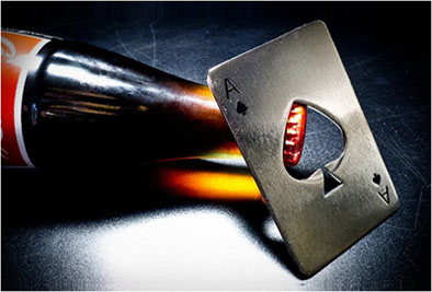 A brass bottle opener shaped like an Ace of Spades playing card with dark patina.