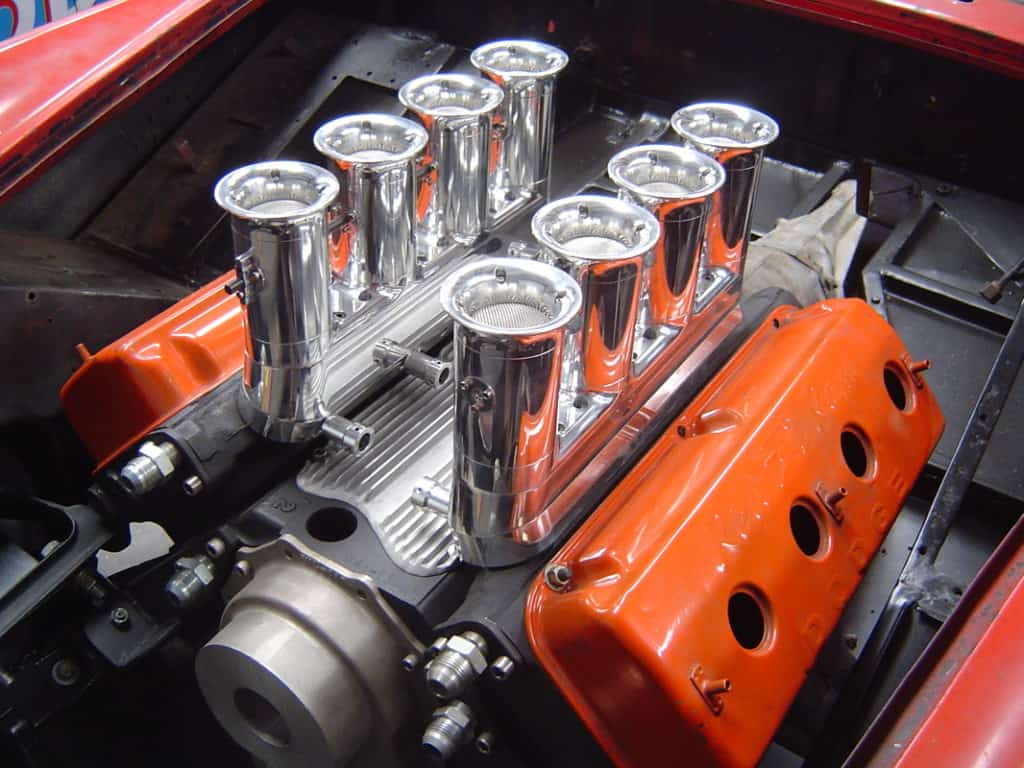 Classic American muscle car engine block with chrome-plated manifold and orange valve covers.