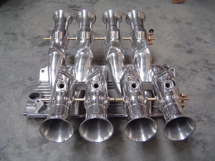 Shiny chrome-plated intake manifold with four trumpet-shaped air induction components.