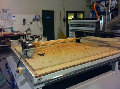 A CNC machine with a 4th axis is woodworking on a piece of wood.