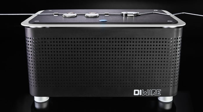 Black rectangular device with silver border and perforated sides featuring circular dials, thin wire, and small blue light on a black background.