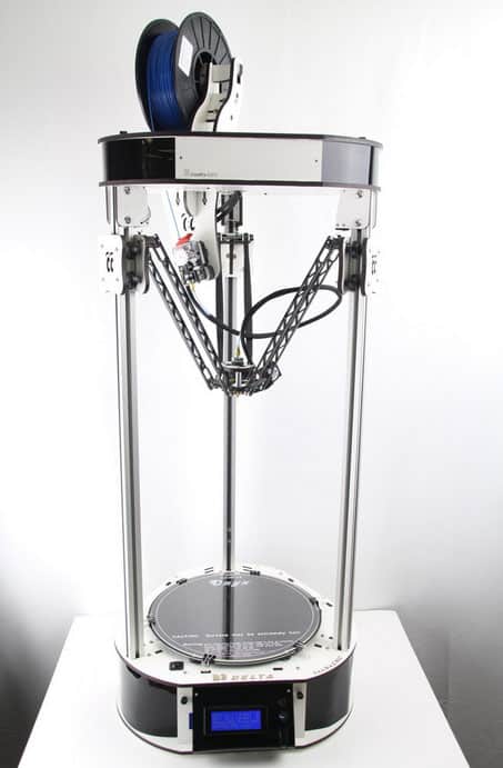 A large 3D printer with black and blue filament spool on top, sitting on a white table against a plain background, with digital display screen.