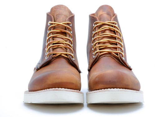 A pair of new brown leather boots with white soles and yellow laces, viewed from the front, against a white background.