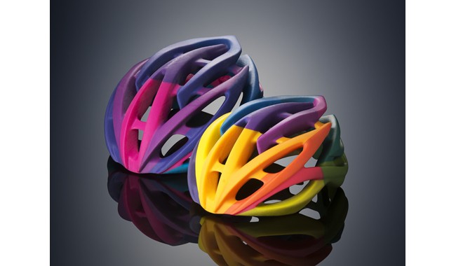 Two colorful bicycle helmets on a Tony Stark Inspired Workshop reflective surface.