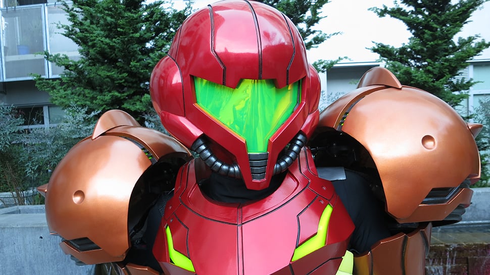 A superhero in a red and green costume is standing in front of a building.