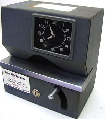 A black clock sitting on top of a white surface in a bustling shop operating multiple shifts.