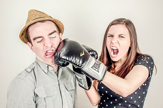 A man is delivering powerful punches to a woman wearing boxing gloves.