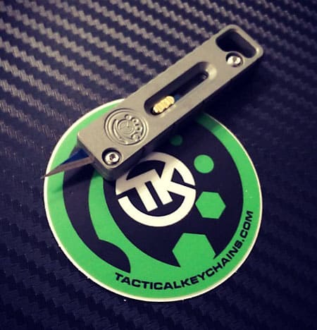 A green and black logo keychain with white TK initials on a green bordered sticker.