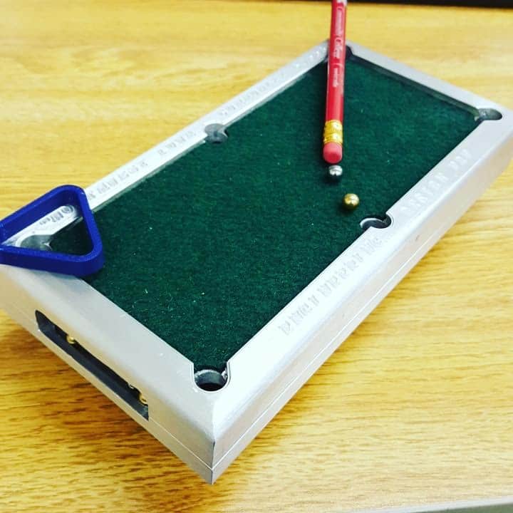 Miniature pool table with a red cue and two balls on a wooden surface.