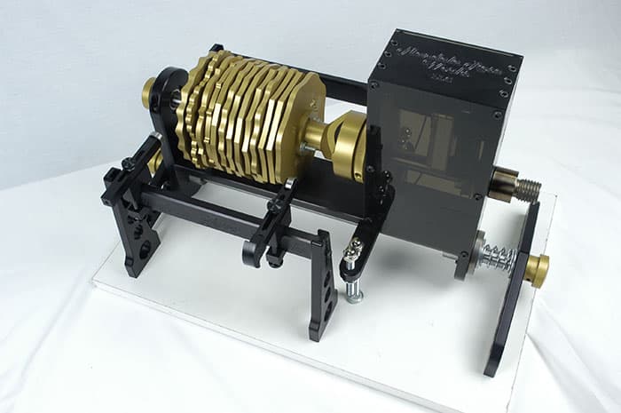 Black and gold cylindrical device with concentric rings on a black base plate against a white background.