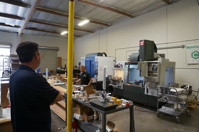 Man in navy blue polo shirt standing in a well-lit metal fabrication workshop.
