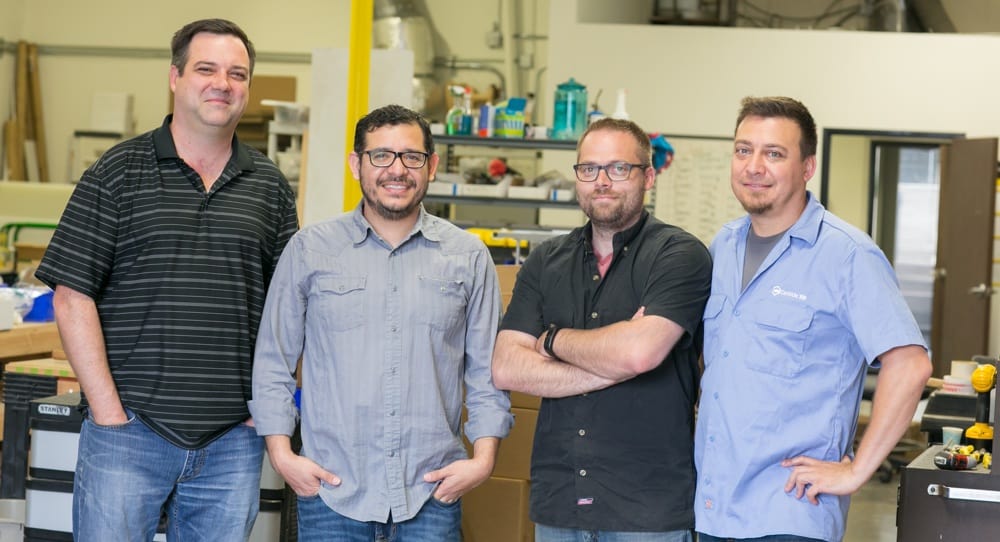 Four men from Southern California standing together in a Carbide3D factory as part of a visit.