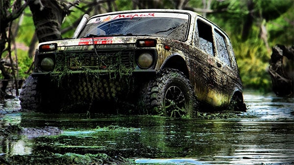 Rugged off-road vehicle navigating through muddy terrain with tires deeply embedded in the mud.