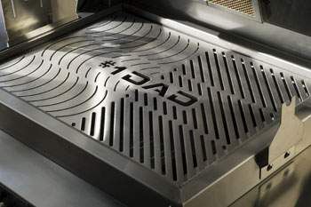 A stainless steel BBQ grill with "#1 DAD" engraving and parallel grooves for heat distribution.
