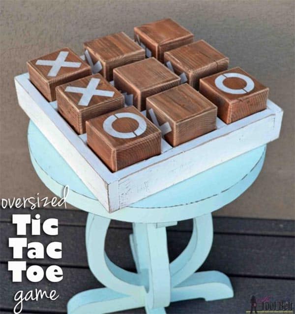 Oversized wooden Tic Tac Toe game with white painted "X" and "O" blocks on gray wall.