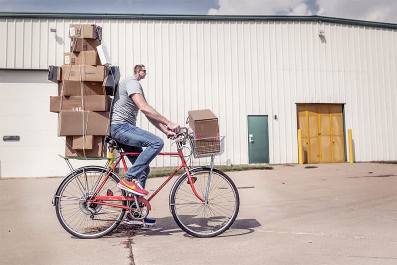 A man hustling harder is riding a bicycle with boxes on his back, getting the job done.