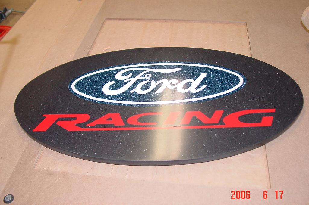 Black oval sign with Ford logo and "Racing" in red text.