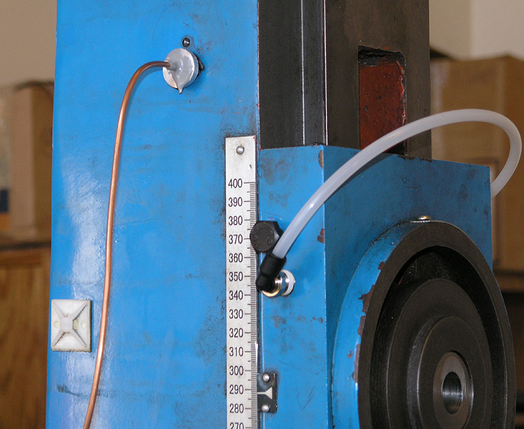 Blue metal device with copper tube, white hose, ruler, and black wheel.