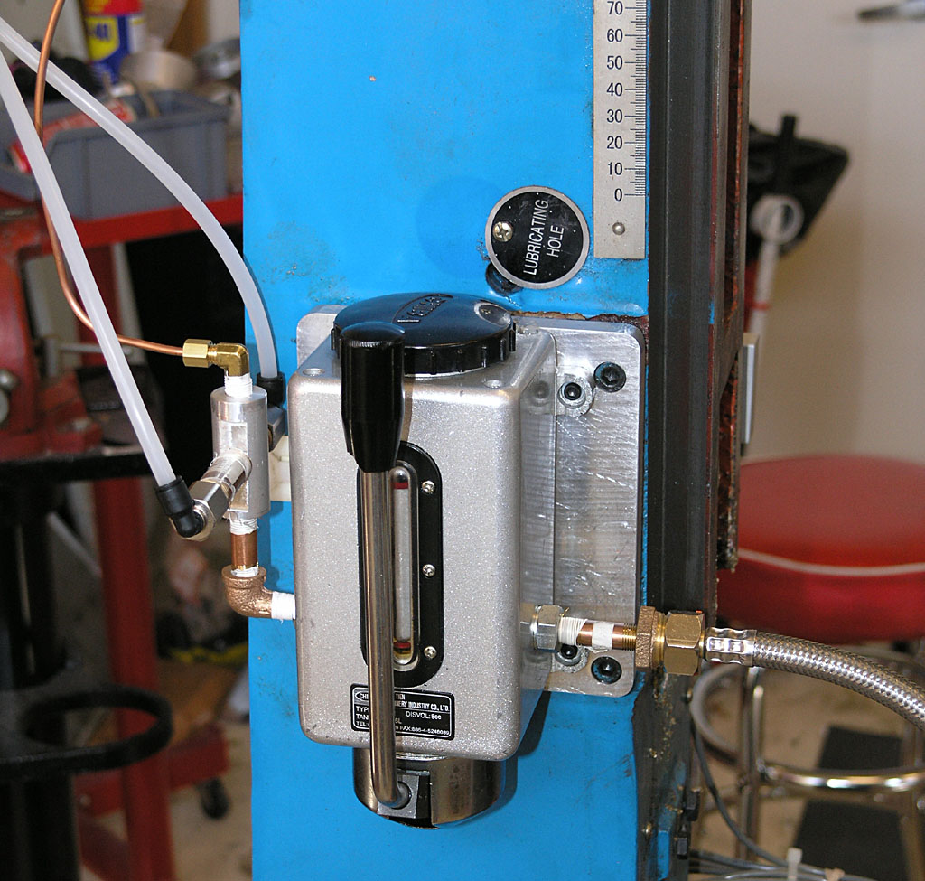 Blue wall-mounted device with pipes, black knob, copper and white tubes, silver body, and round gauge.