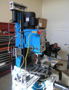Blue and black metalworking machine with table, tools, and workshop setting.