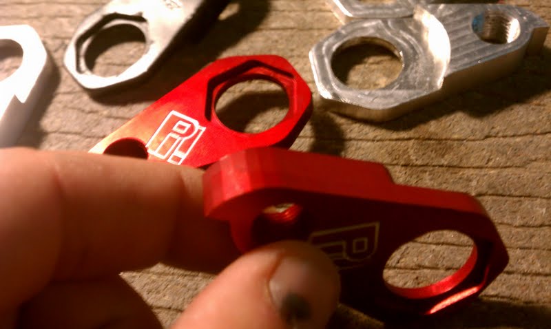 Red and silver metal pieces with holes, possibly for machining or metal fabrication.