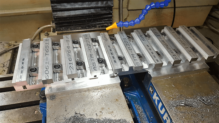 Blue anodized aluminum vise with silver metal clamps on a dirty metal workbench.