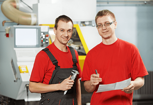 Two men in workshop setting, one in red overalls, other in red t-shirt.