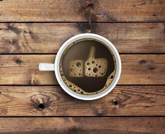 A white coffee cup filled with dark brown liquid and a foam "like" symbol resembling cheese.