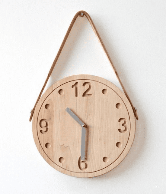 A wooden wall clock with a leather strap hangs on a white wall.