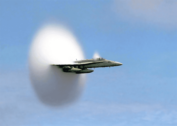 Jet plane flying from right to left in a clear blue sky with white vapor trail.