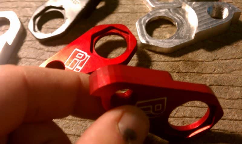 Metal parts and red anodized aluminum part with engraved R on a wooden surface.
