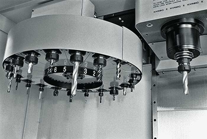 Black-and-white photograph of a machined metal component with circular base and multiple holes.