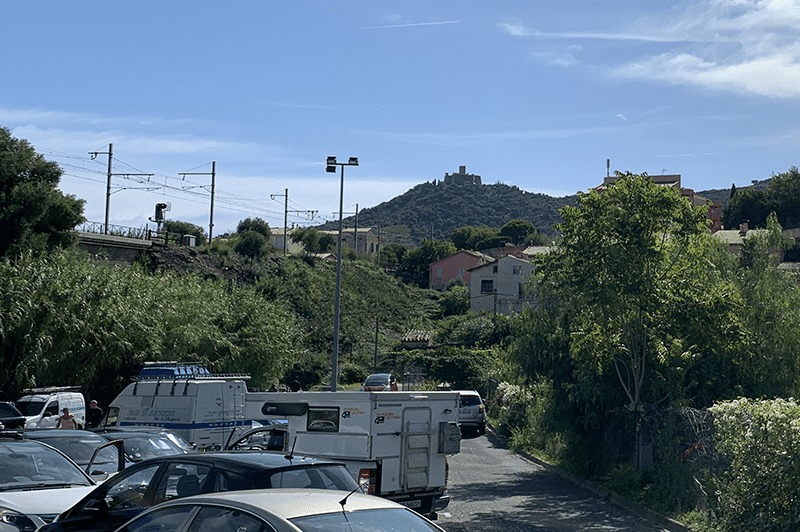 A parking lot scene with cars, trucks, RVs, and mountains in the background.