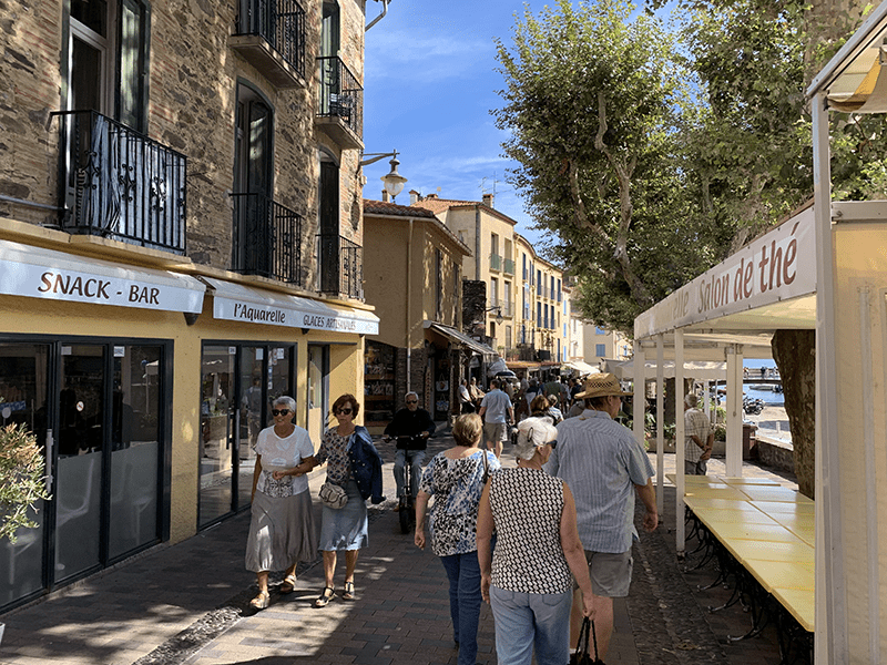 Bustling street scene with old and new buildings, pedestrians, and a sign reading "SNACK BAR" in French.