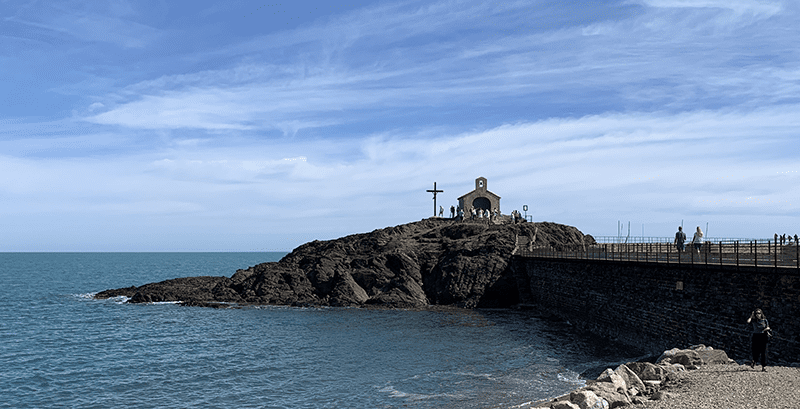 Small church with cross on rocky coast overlooking ocean.