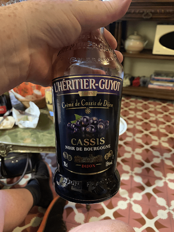 Hand holding a bottle of L'Heritier-Guyot Cassis Noir de Bourgogne wine.