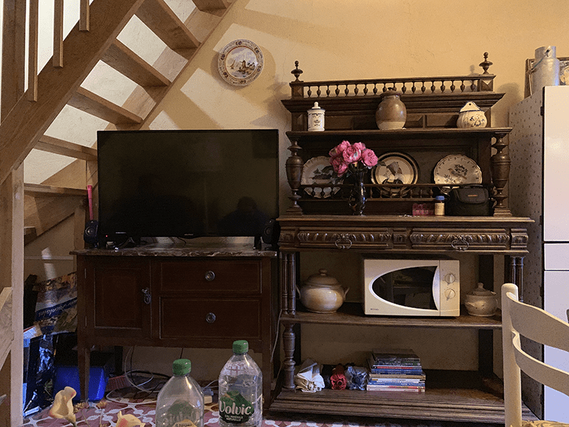 Living room scene with TV stand, shelves, microwave, and household items on a beige background.