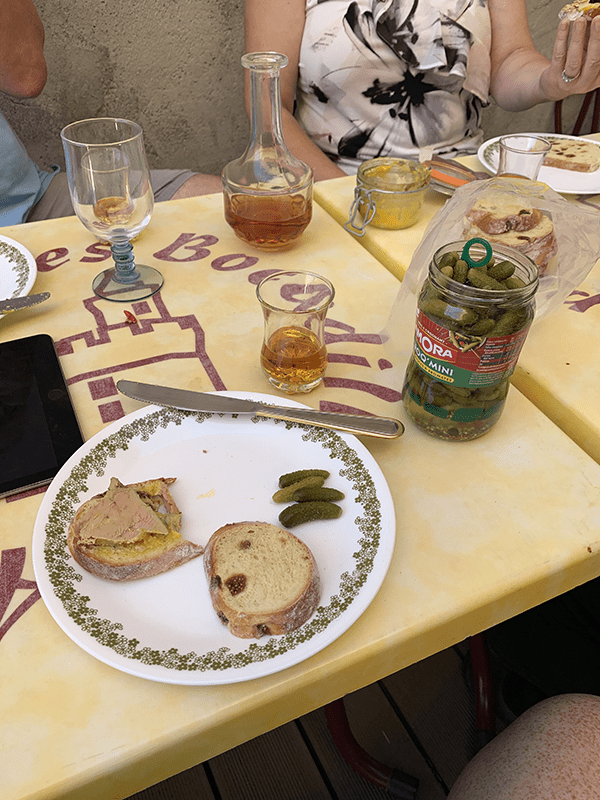 A yellow table with food items, including bread slices, pickles, olives, and glasses of beverage.