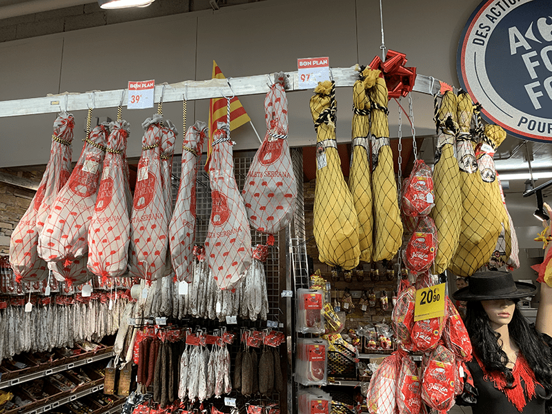 Cured meats on display in a store setting, packaged with red designs and price tags.