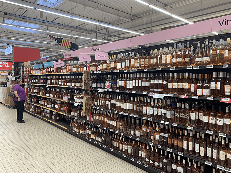 Supermarket aisle with rows of wine bottles on clean white-tiled floor.