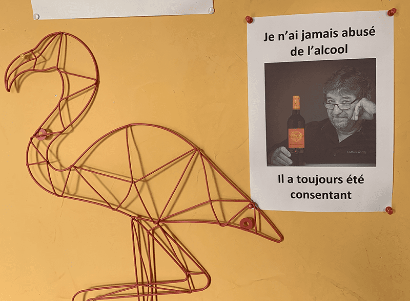 Wire sculpture bird next to black-and-white photo of man with orange-labeled bottle, French text.