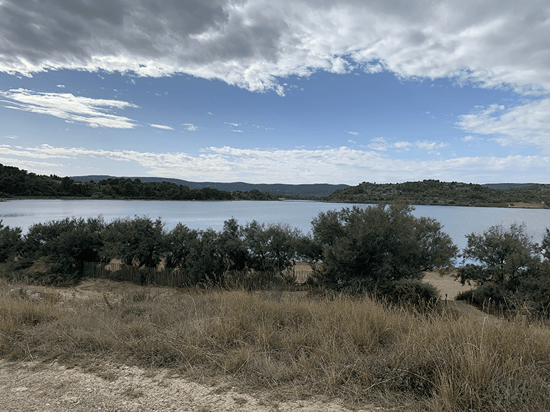 Landscape photograph of a serene lake surrounded by trees under a cloudy sky with calm water reflecting the blue sky above.