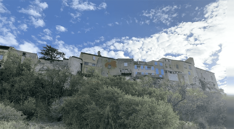 A serene hilltop landscape with an old stone building, lush greenery, and blue skies.