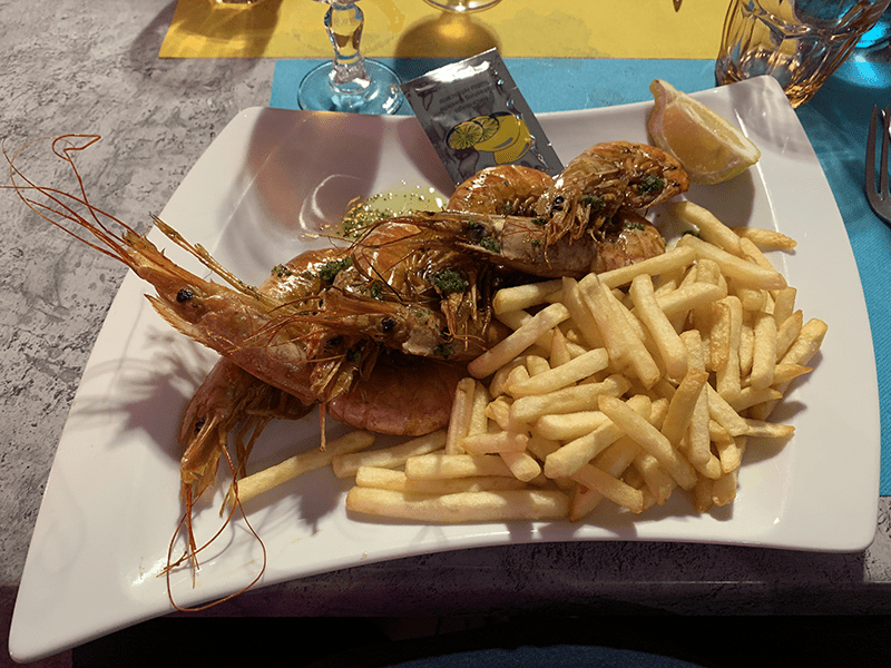 Two large prawns on a plate with fries and lemon, garnished with condiment packaging.